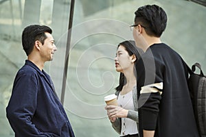 Three young asian adults standing talking on street