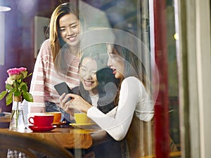 Three young asian women looking at mobile phone in coffee shop