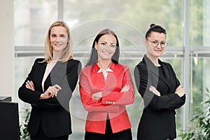 Three young attractive women in business suits posing against the backdrop of a light office. Head and subordinates photo