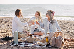 Three young beautiful happy women female friends having cozy summer picnic with lemonade, fresh bread and fruits on a beach