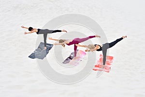 Three young beautiful women perform virabhadrasana yoga pose