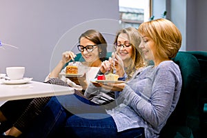 Three young beautiful Women sitting on the sofa in cafe indoors and Having lunch In Cafe. Women eating cakes and having