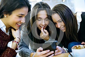 Three young beautiful women using mobile phone at cafe shop.