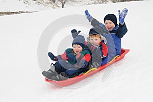 Three young boys sledding downhill together