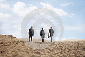 Three young business people walking through the desert, rear view, distant