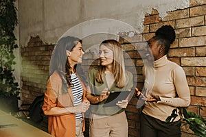 Three young business women with digital tablet standing by the brick wall in the industrial style office