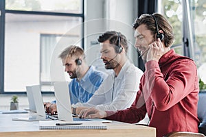 three young call center operators in headsets using laptops