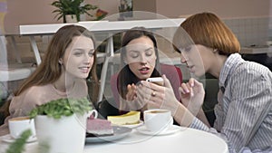 Three young caucasian girls are sitting in a cafe, laughing, smiling, friends, company, gossips, dialogue, discussion