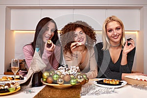 Three young cheerful intercultural women with alcoholic drinks standing in front of camera while enjoying home party in