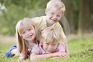 Three young children playing outdoors smiling