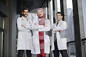 Three young confident Saudi Arab doctors, standing outside the hospital and looking at camera