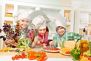 Three young cooks cutting pizza at the kitchen