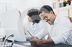 Three young coworkers working together in a modern office.African american man in white shirt smiling in workplace.