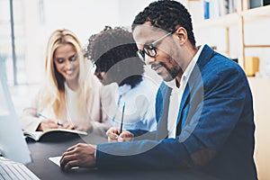 Three young coworkers working together in a modern office.Man wearing glasses, jacket and making notes in document.Horizontal,blu