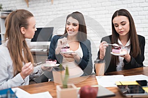 Three young cute girls eating sweet cake at lunchtime in office. Lunch break.