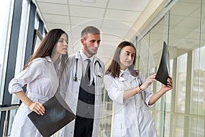 Three young doctors discusses the results of an MRI scan of the patient`s head in modern hospital hallway