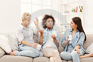 Three young female friends with coffee chatting at home