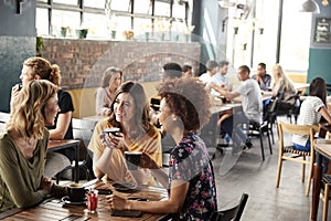 Three Young Female Friends Meeting Sit At Table In Coffee Shop And Talk photo