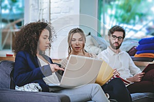 Three young friends friends students sitting seated onsofa in room