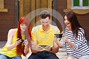 Three young friends laughing watching video on mobile phone outd