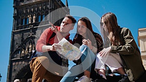 Three young friends navigate the map and looking right path under the old tower. Czech, Prague