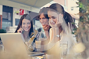 Three young friends shopping online in cafe on laptop.