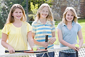 Three young girl friends on tennis court smiling