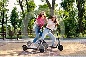 Three Young girl friends on vacation having fun driving electric scooter through the city park. Ecological and urban city