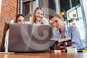 Three young girlfriends talking online lesson using a laptop sitting in a library