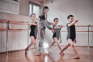 Three young girls have a ballet training with their attractive teacher