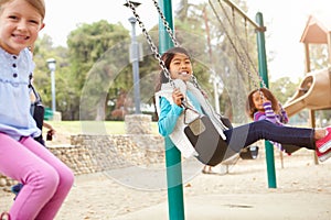 Three Young Girls Playing On Swing In Playground