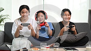 Three young girls playing video games together on sofa at home.