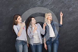 Three young girls pointing up on grey background