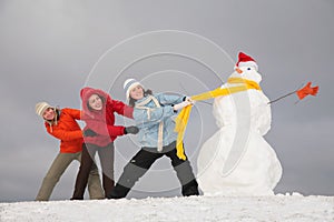 Three young girls pull snowman by scarf