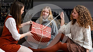 Three young girls sitting on the couch and having fun unwrapping Christmas presents at home