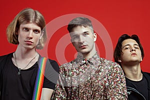 Three young handsome men of different nationalities stand on vibrant red background.