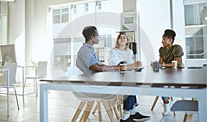 Three young happy businesspeople having a meeting while sitting at a table at work. Business professionals talking and