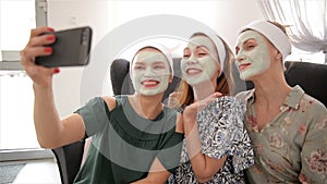 Three young happy women with face masks taking selfie at spa resort. Friendship and wellbeing concept, health beauty