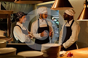 Three young intercultural cooks in uniform discussing working points