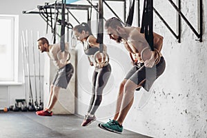 Three young male and female adults doing pull ups on rings