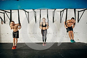Three young male and female adults doing pull ups on rings