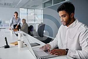 Three young multiracial business people in businesswear working on laptops at desk in office