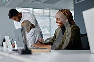 Three young multiracial business people in businesswear working at desk on laptops in office photo