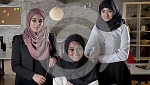 Three young muslim womens in hijab looking in camera and smiling in modern office, black muslim women with colleagues at