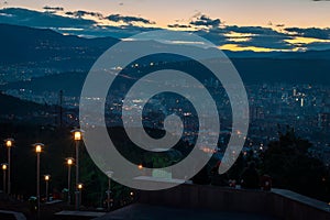 Three young people sitting on top of the hill overlooking the capital of Georgia, Tbilisi while the sun goes down behind the hill