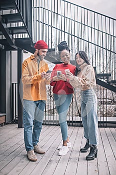 Three young people with smartphones near office