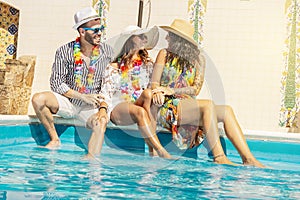 Three young people smiling sitting on the edge of a swimming pool