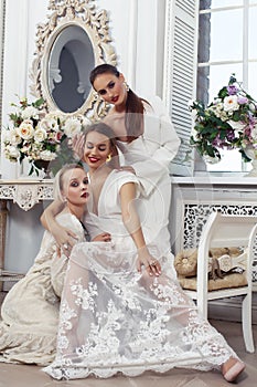 Three young pretty lady in white lace fashion style dress posing in rich interior of royal hotel room, luxury lifestyle