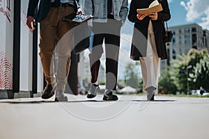 Three young professionals walking in a city with digital devices and notebooks