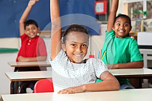 Three young school children arms raised in class